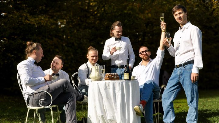 Die Musiker bei einem Picknick im Grünen, am gedeckten Gartentisch, bei guter Stimmung.