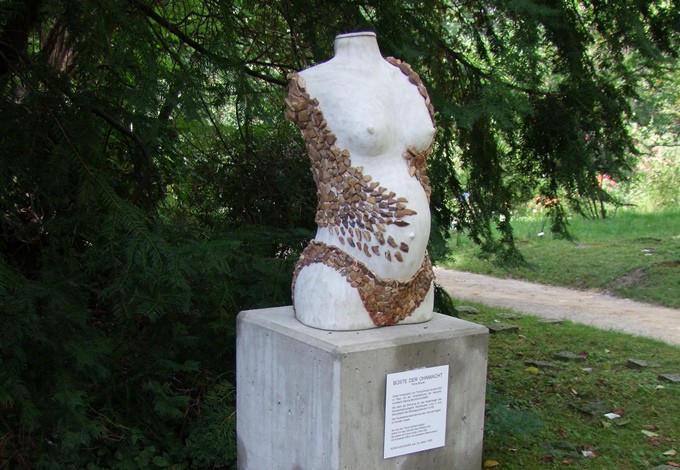 Steine bedecken teilweise den nackten Oberkörper einer schwangeren Frau.